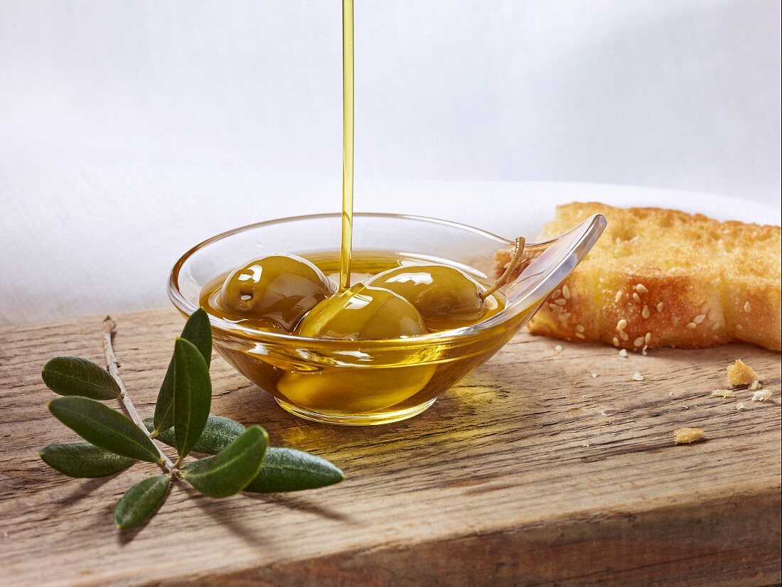 Olive oil being poured over green olives in a small dish