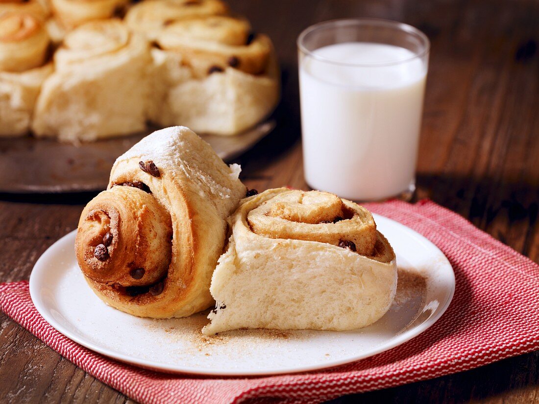 Two cinnamon buns on a plate served with a glass of milk