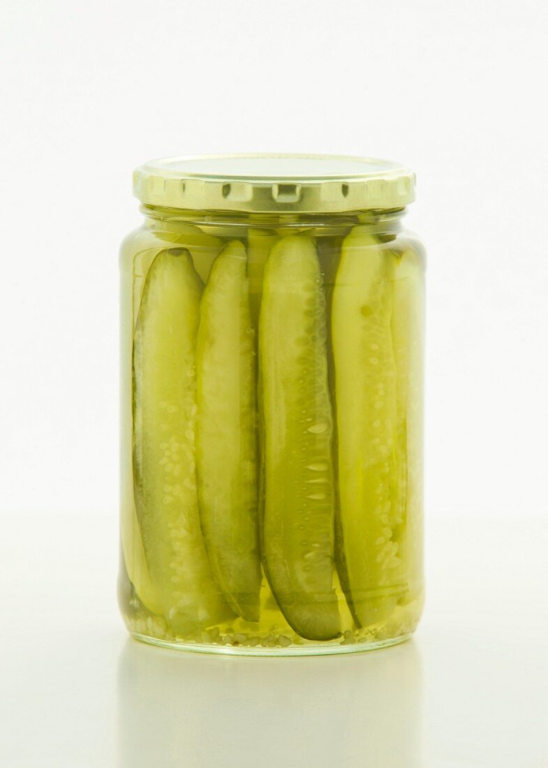 Sliced gherkins in a screw-top jar on a white surface