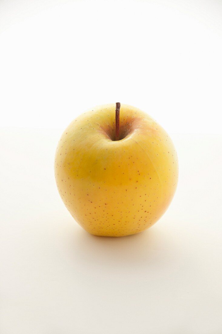 A yellow Golden Delicious apple on a white surface