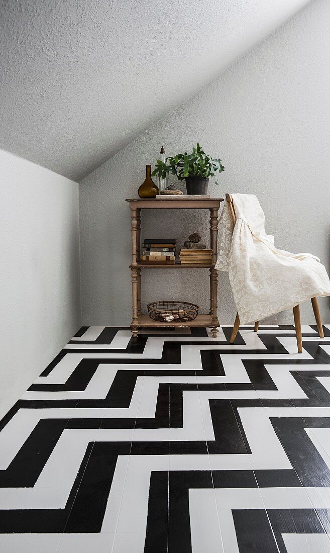 Books and house plant on open-fronted, vintage shelf unit on wooden floor painted with black and white zigzag pattern