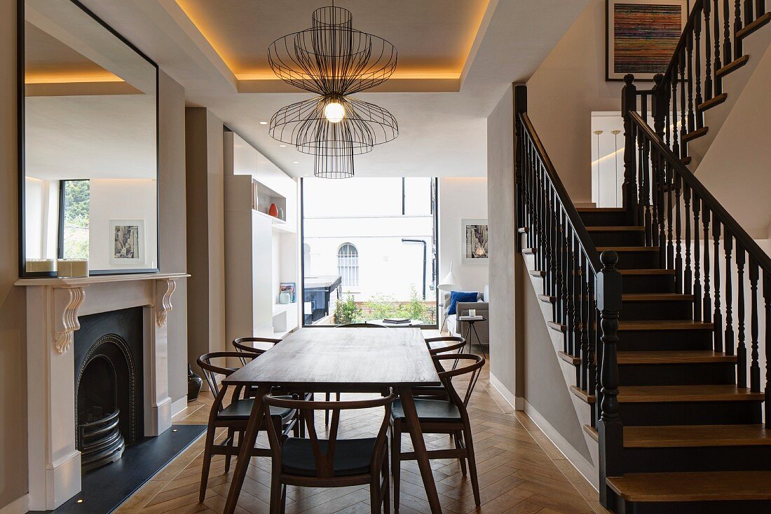 Elegant, restored wooden staircase with black-painted balustrade in open-plan interior with fireplace and modern, panoramic window