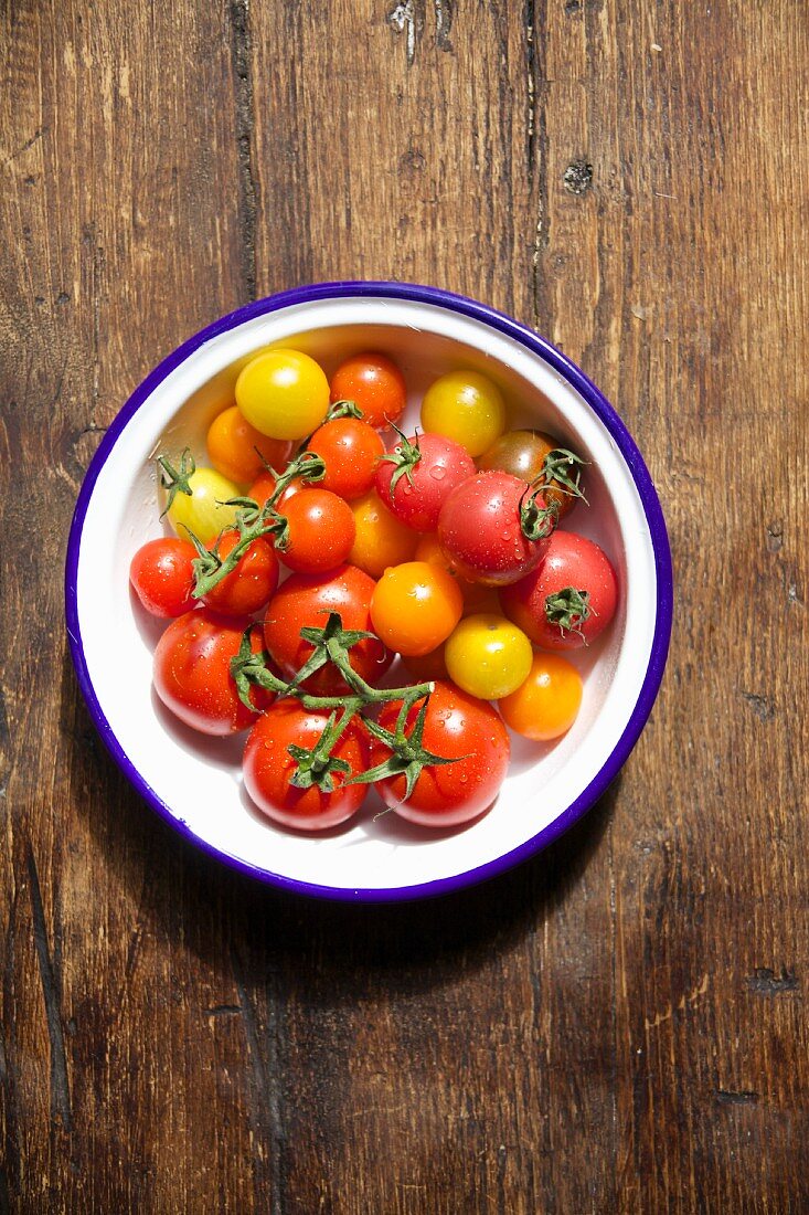 Various tomatoes in a bowl on a wooden table