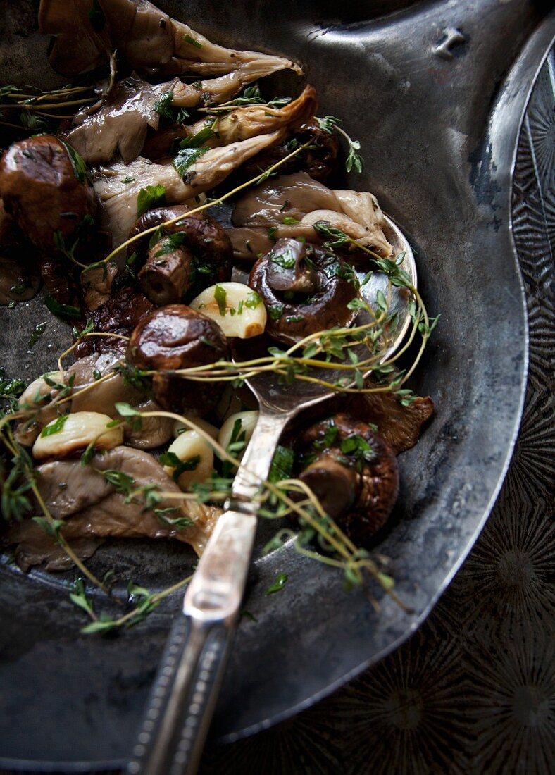 Various types of roasted mushrooms with garlic and thyme in an antique pan