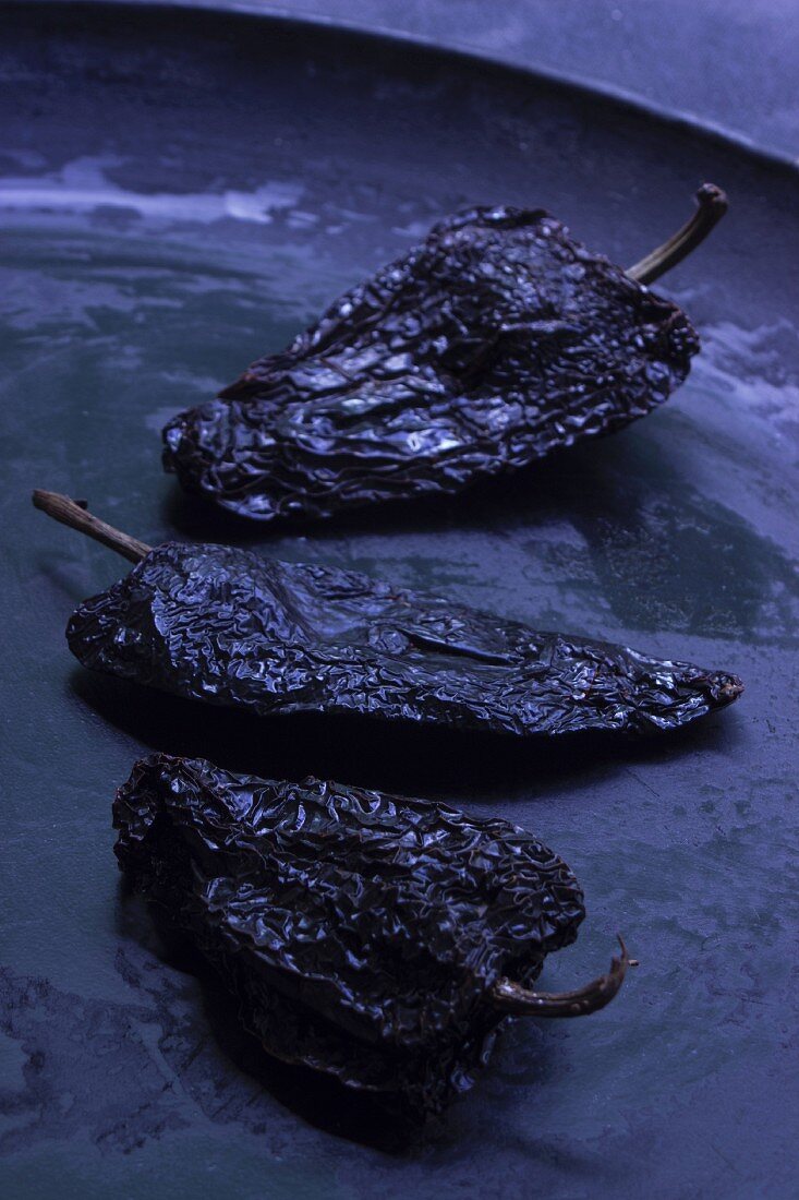Drei schwarze Jalapeno-Chilischoten auf schwarzer flacher Schale