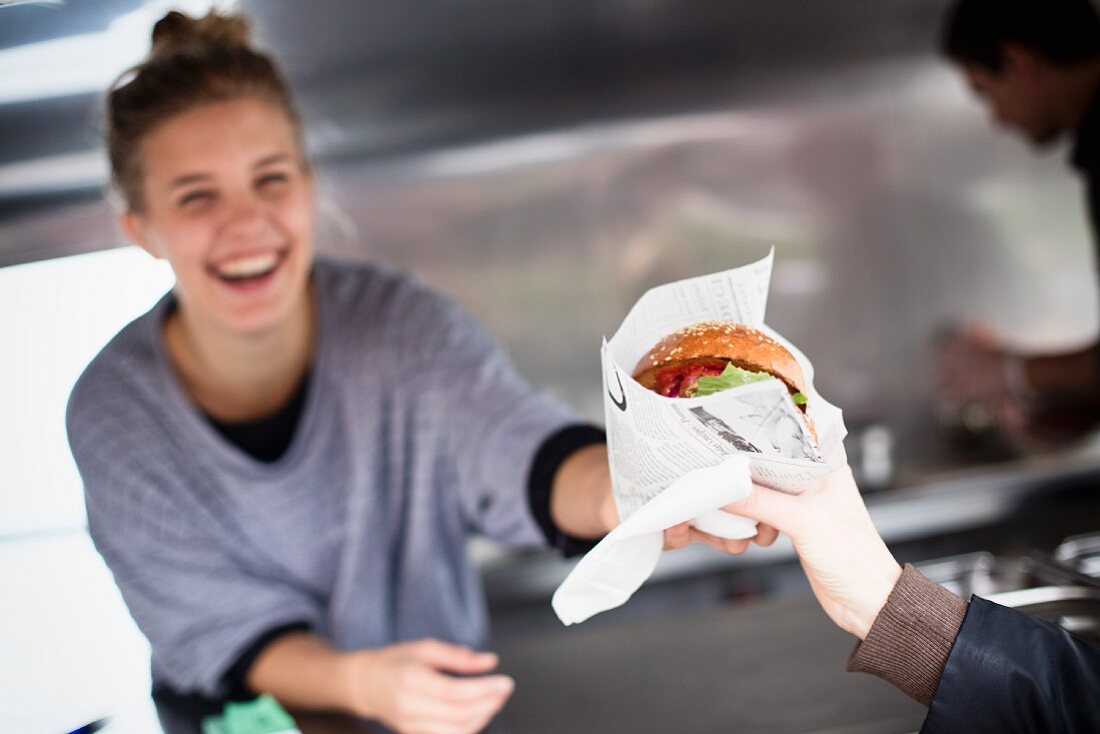 A laughing young woman selling a hamburger