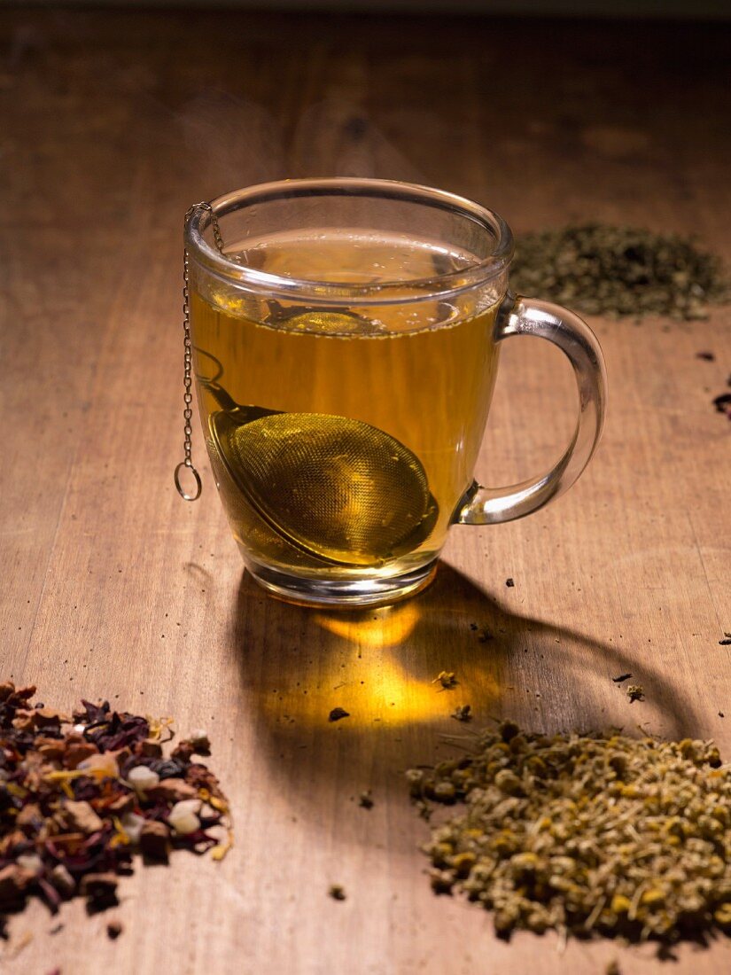 A tea infuser with herb tea in a glass cup