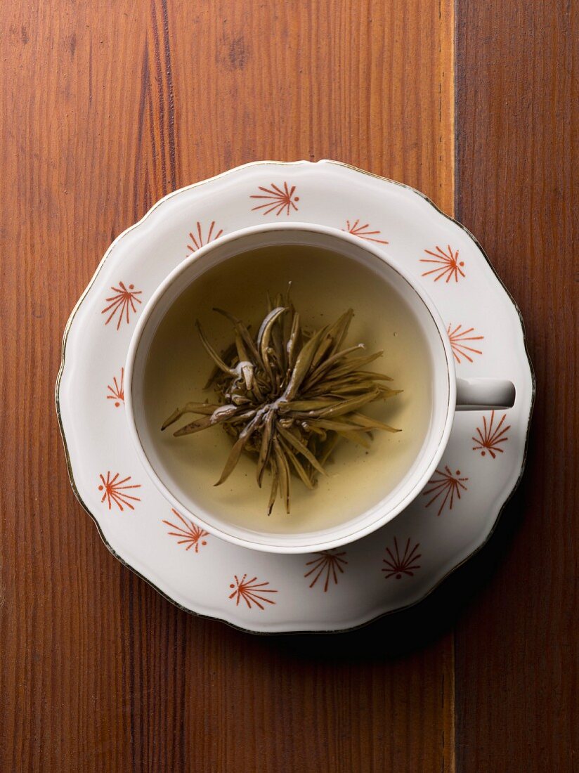A cup of herb tea with the tea flower on a wooden table