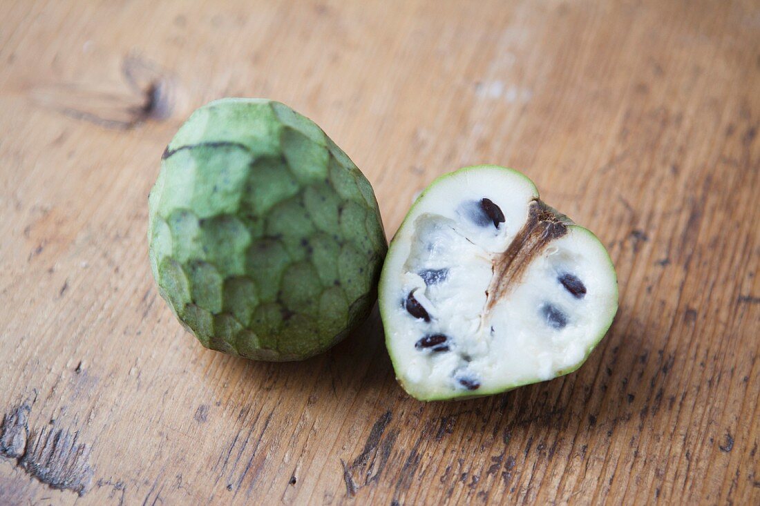 Whole and halved cherimoya on a wooden table