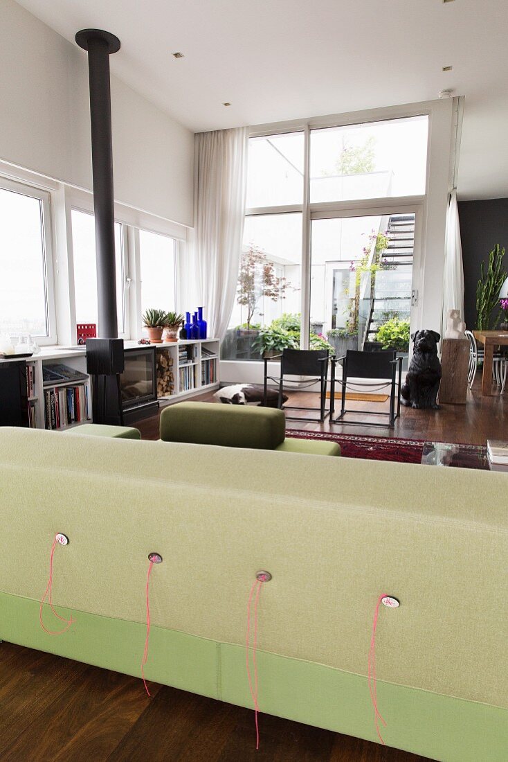 Backrest of lime-green sofa in open-plan interior with chairs in front of glass wall