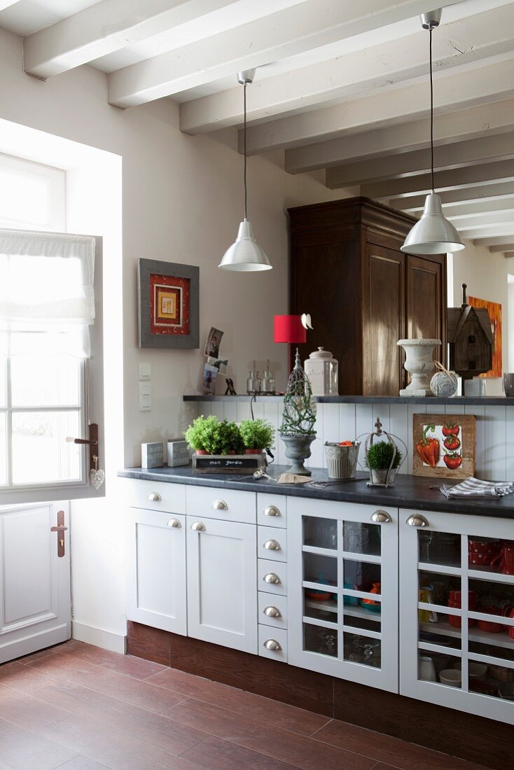 Kitchen counter with white, country-house-style base units and raised bar below pendant lamps