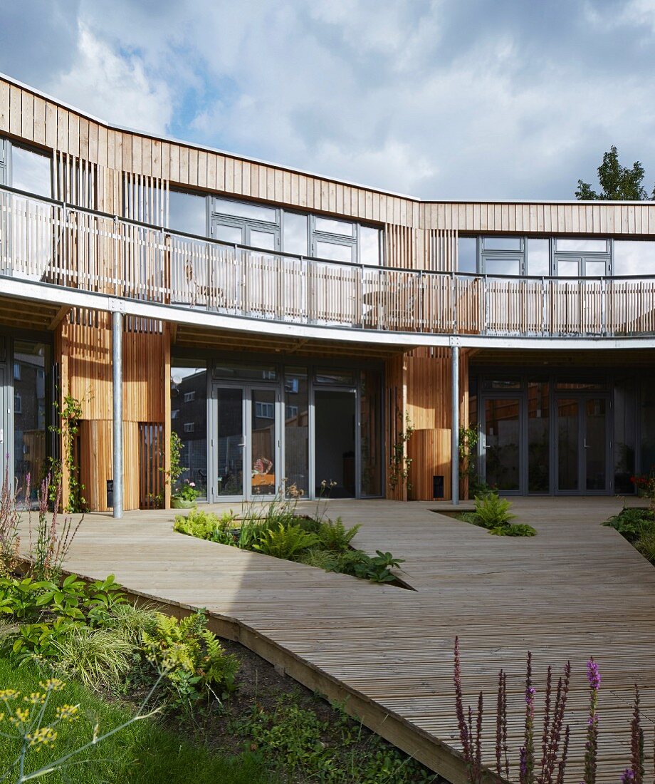 Modern, shared eco-home with encircling balcony and wooden deck in entrance area