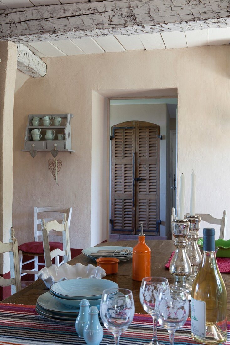 Glasses and crockery on table in front of open door with view of cupboard with rustic, slatted wooden door