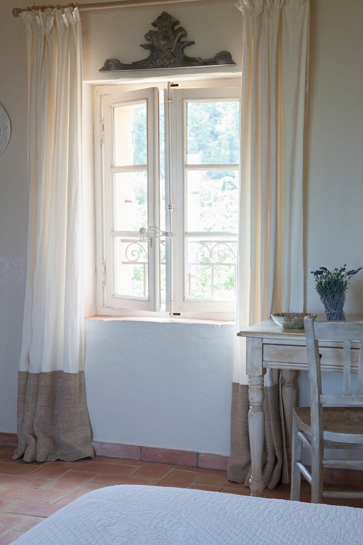 Floor-length curtains on open lattice window and vintage desk and chair in bedroom