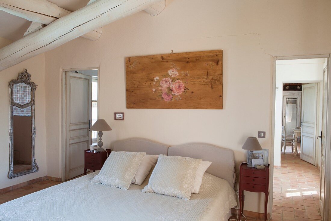 Doppelbett mit drapierten Kissen unter massiven Holzbalken, seitlich offene Türen und Blick in Nebenzimmer