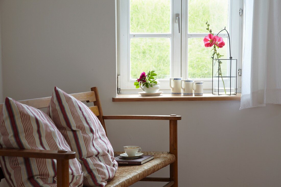 Cushions and cup of tea on wooden bench below window