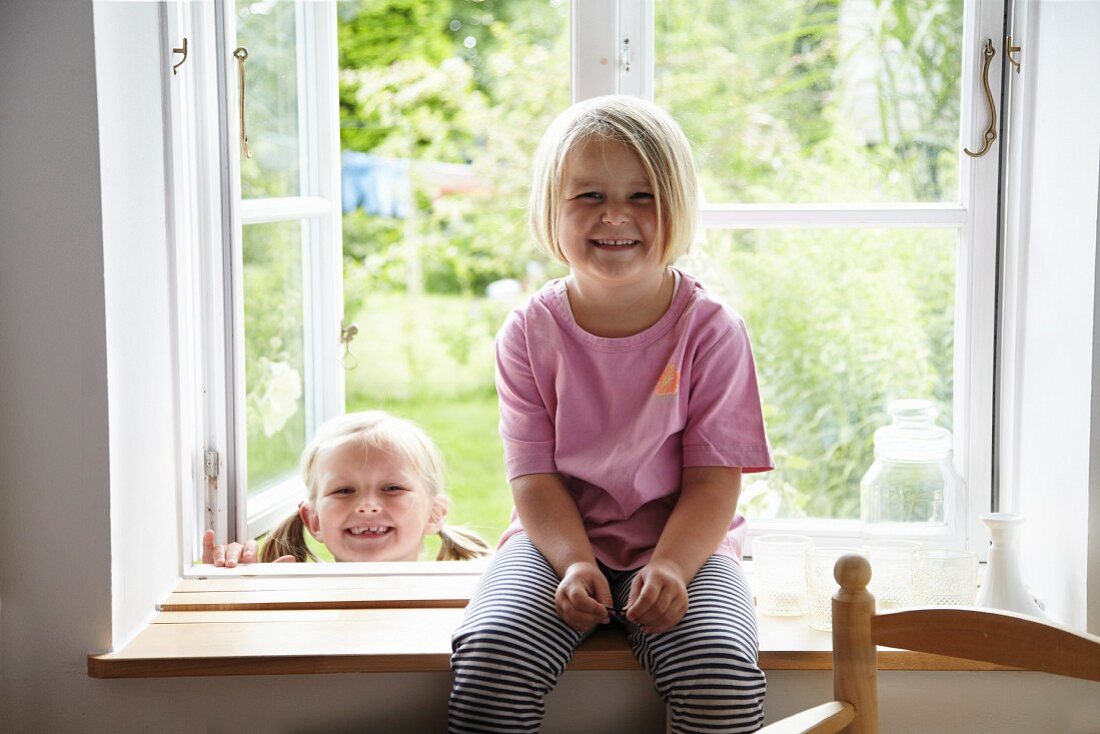 Two blonde girls in window with view of garden