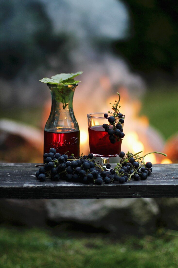 Selbstgemachter Wein und rote Trauben vor einem Lagerfeuer