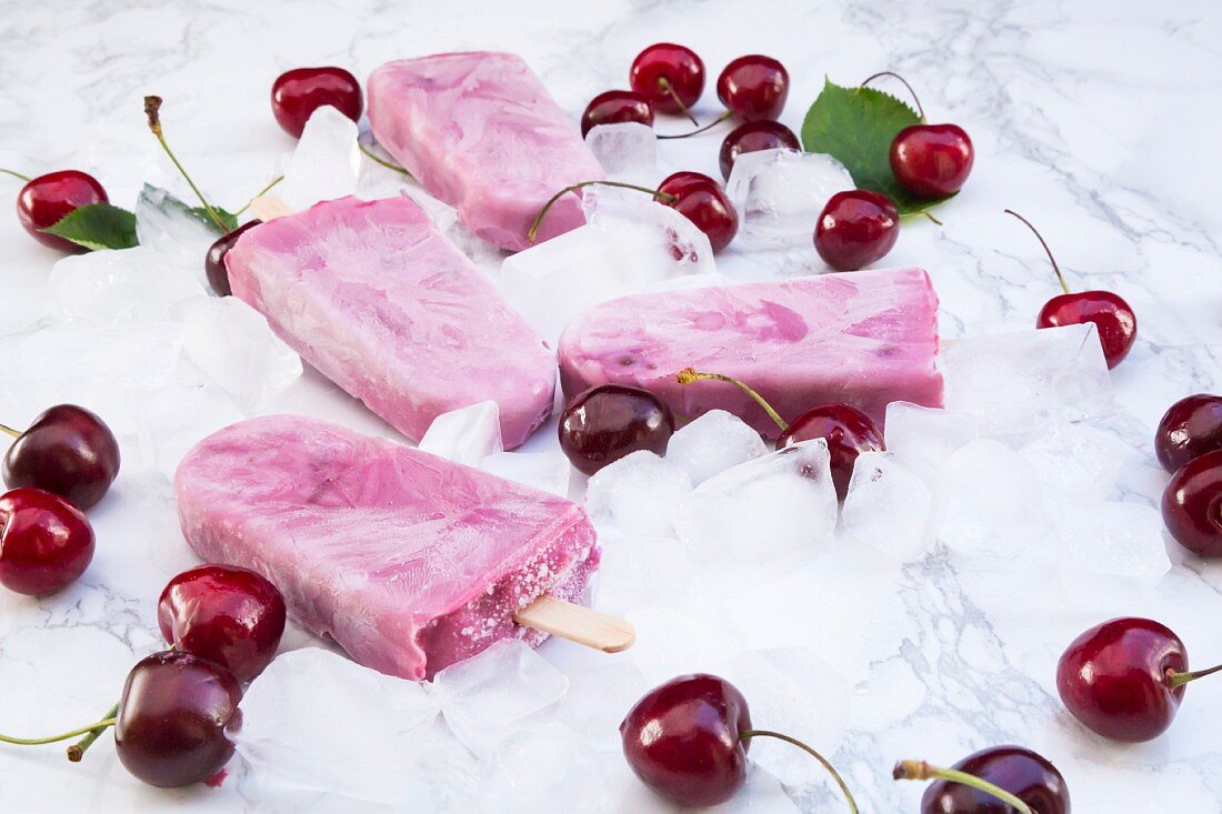 Cherry and yoghurt ice cream sticks surrounded by fresh cherries and ice cubes