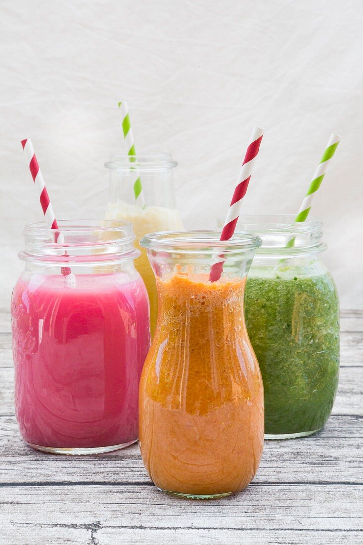 Vier verschiedene Smoothies in Gläsern mit Strohhalmen