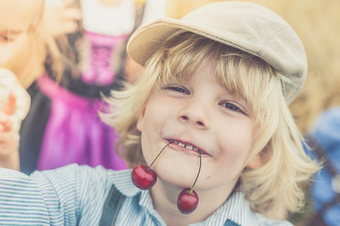 A blond boy holding two cherries in his mouth