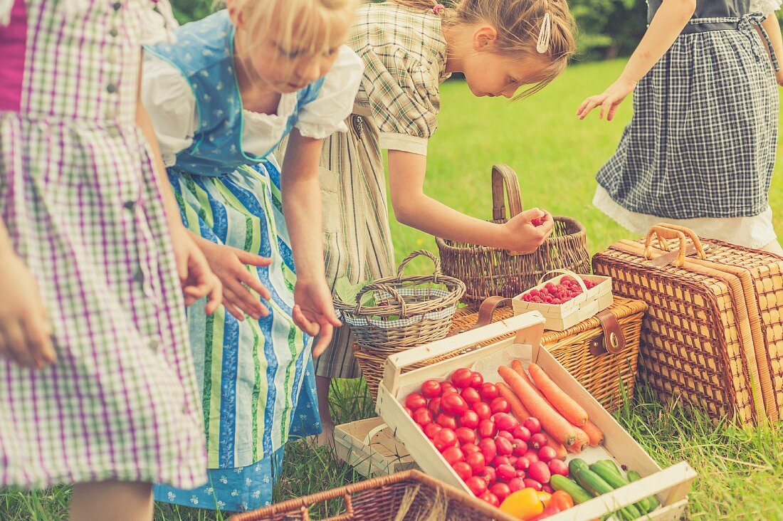 Mädchen in Trachtenkleidern mit frisch geerntetem Obst & Gemüse auf Wiese