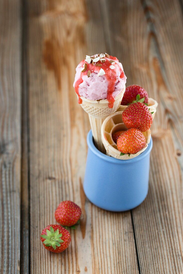 Strawberry ice cream with strawberry sauce and chopped hazelnuts in an ice cream cone