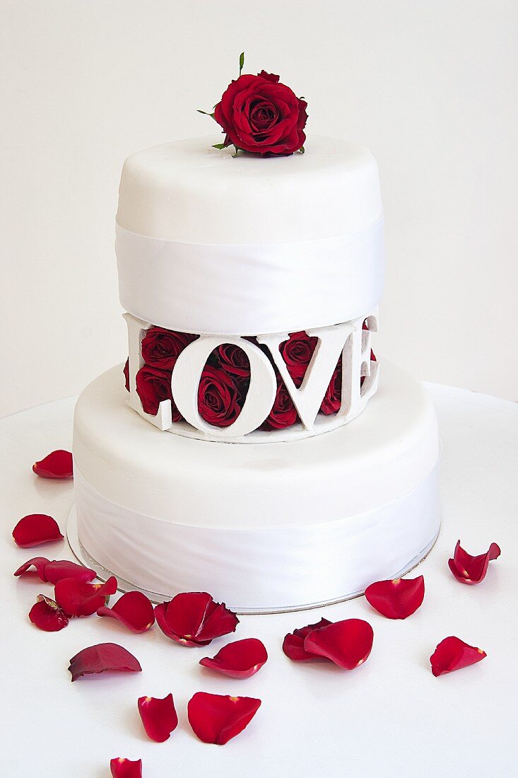 A two tier wedding cake with with red rose petals