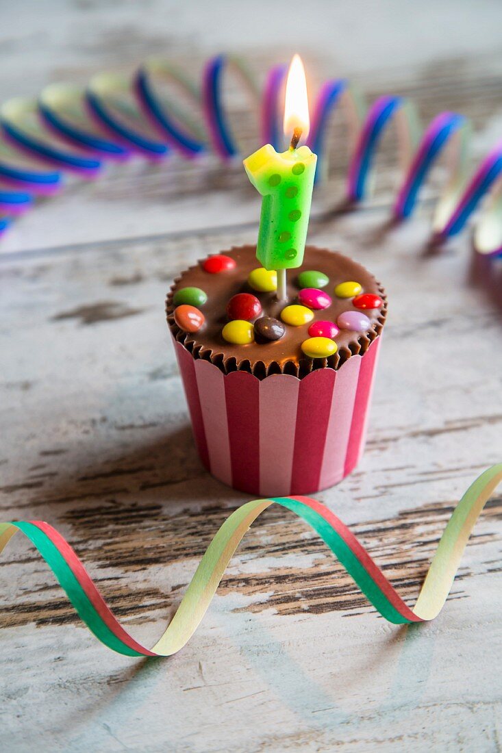 A birthday muffin decorated with chocolate beans and a candle