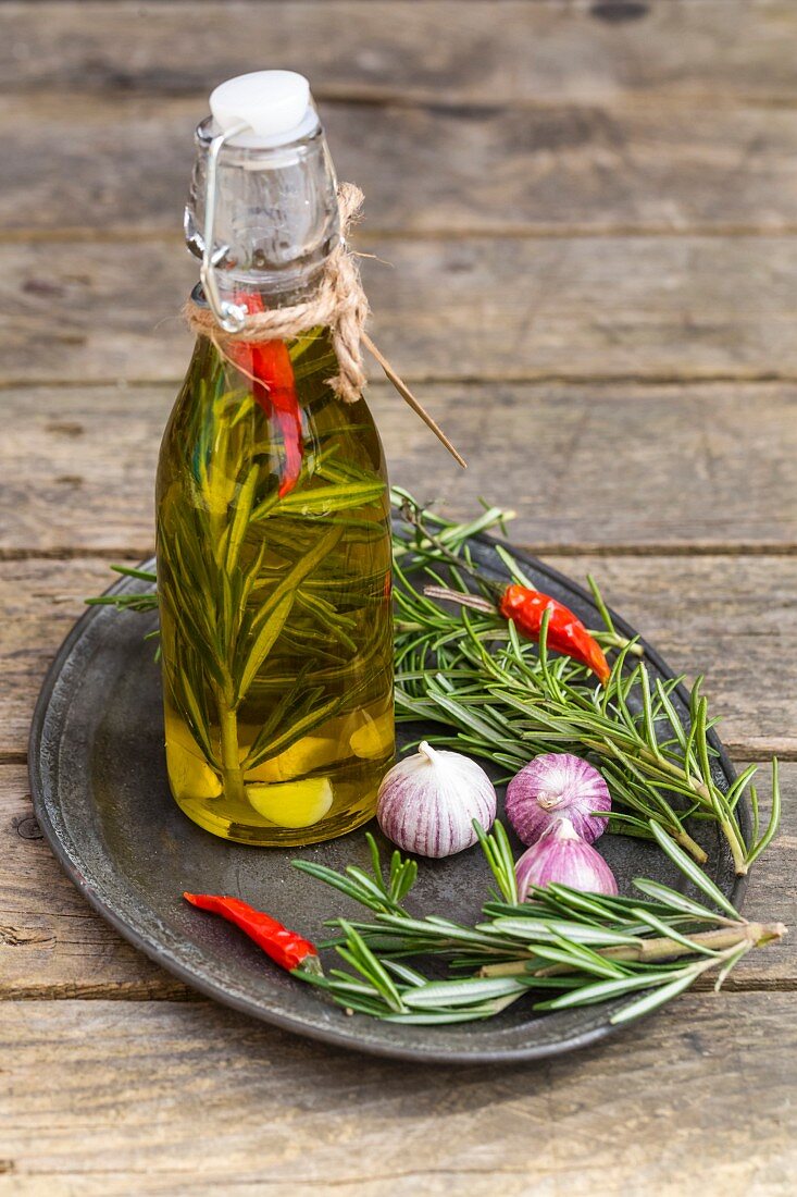 Olivenöl mit Rosmarin, Knoblauch und Chilischoten in Flasche auf Holztisch