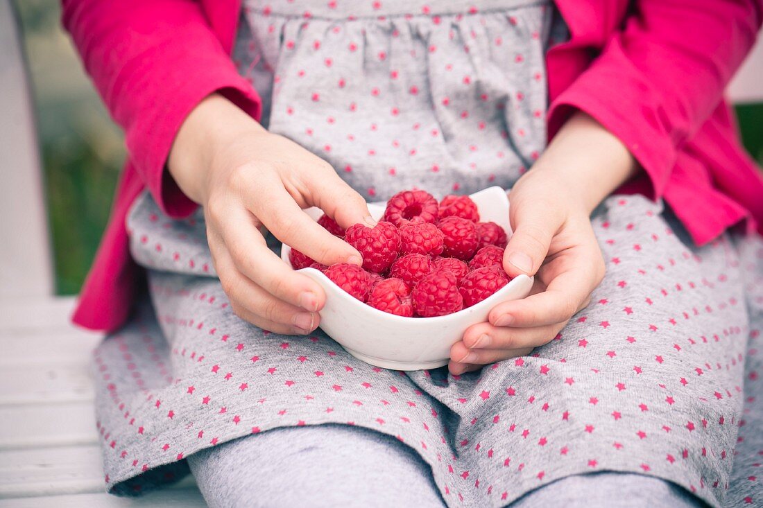 A little girl holding a bowl of fresh strawberries