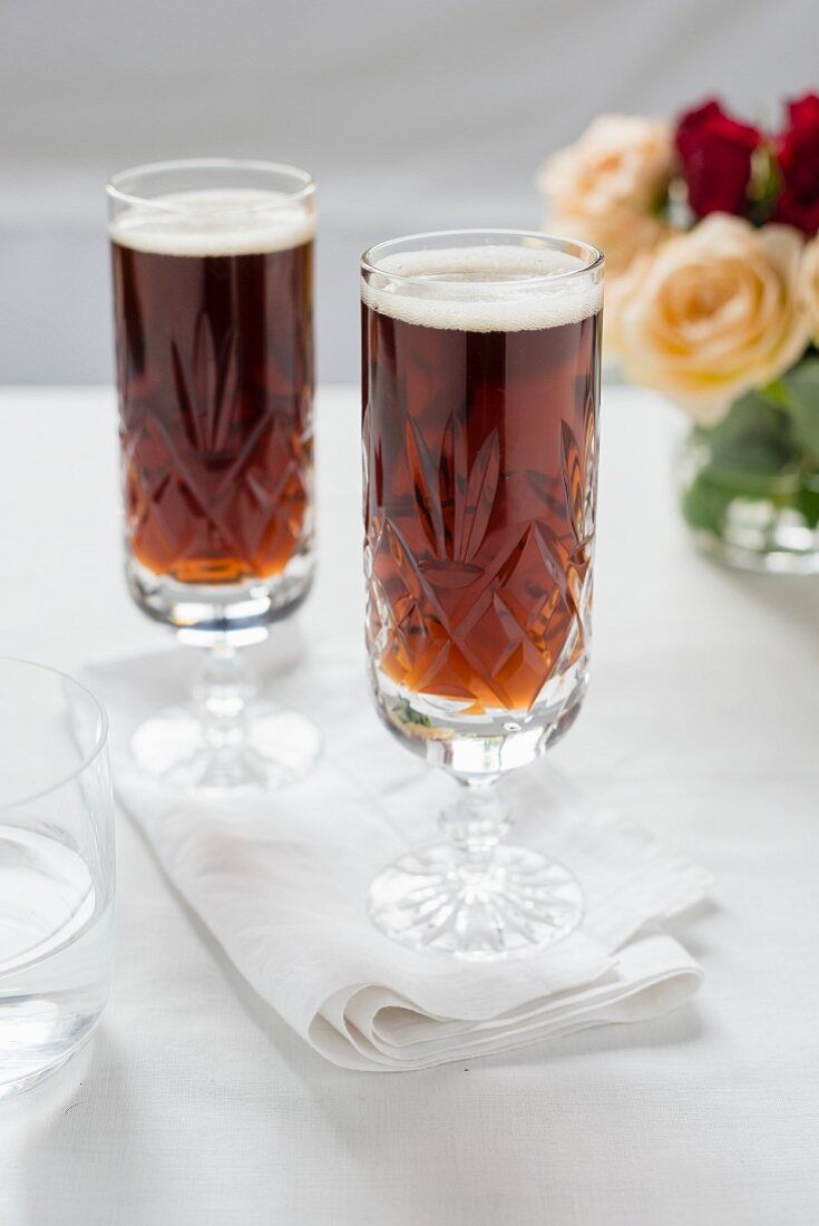 Zwei Gläser dunkles Bier vor einem Rosenstrauss