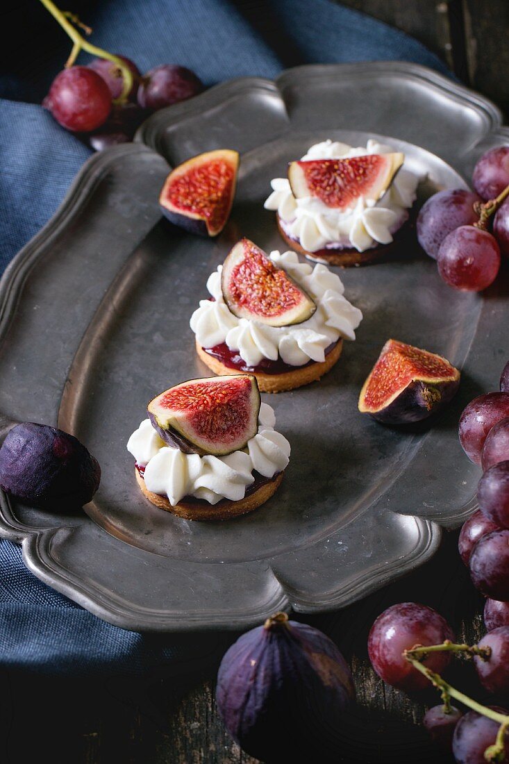 Mini cakes with sliced figs and whipped cream on an old serving platter