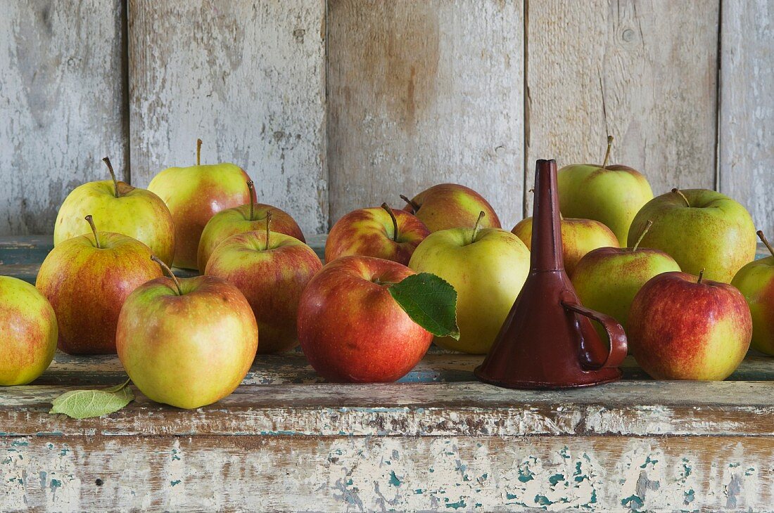 A funnel and Jonagold apples on a rustic shelf