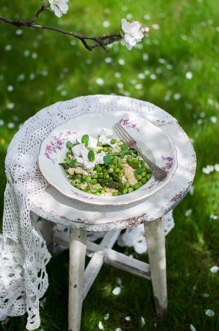 Hirsesalat mit Spargel, Erbsen, Ziegenkäse und frischer Minze auf altem Gartenstuhl