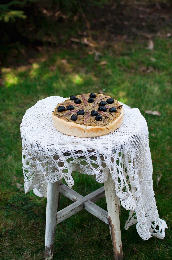 Pissaladiere (Pizza mit karamellisierten Zwiebeln, Sardellen und schwarzen Oliven, Frankreich) auf altem Gartenstuhl