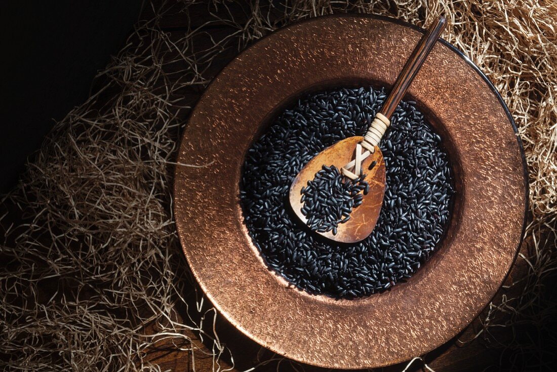 Black rice in a copper dish with a wooden spoon seen from above