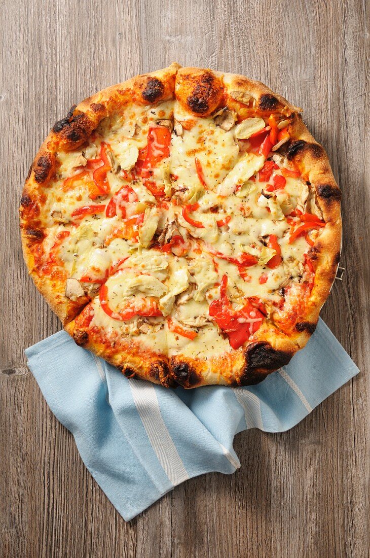 Pizza mit Tomaten und Artischocken auf Holzuntergrund