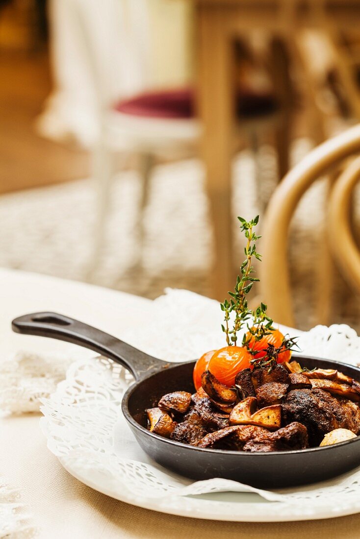 Schweinefleisch mit Tomaten in gusseiserner Pfanne auf Tisch