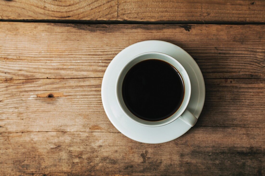 A cup of coffee on a wooden surface (seen from above)