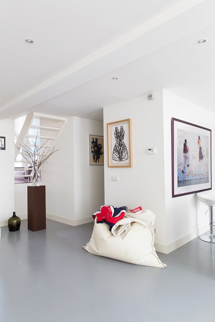 Modern interior with grey epoxy resin floor, white beanbag against wall and framed pictures