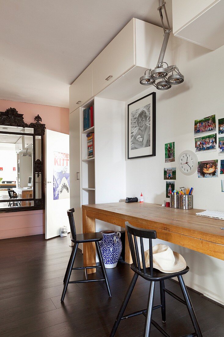 Narrow table made of pale wood and black bar stools below collection of photos on wall