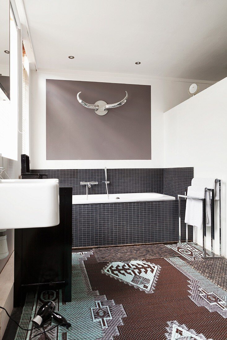Patterned rug, bathtub with black-tiled surround and stylised hunting trophy in modern bathroom