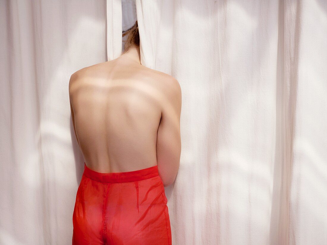 Young topless woman sticking head between curtains