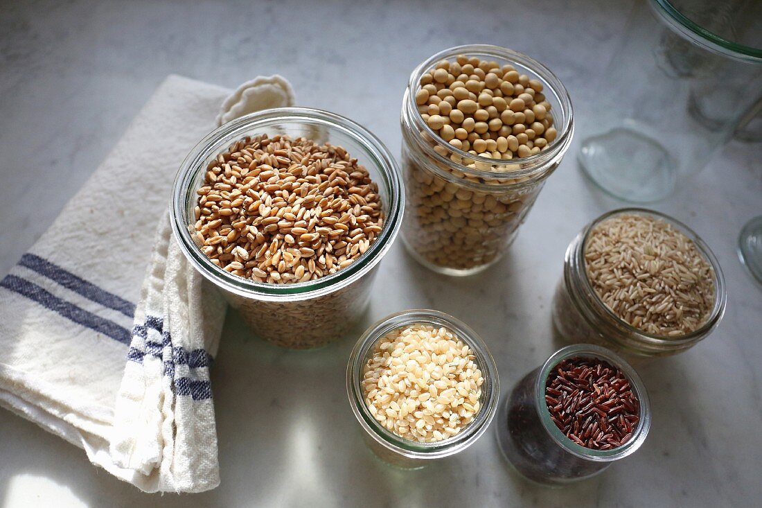 Organic spelt, soya beans, long grain rice, red Himalayan rice and short grain rice in jars on a marble surface