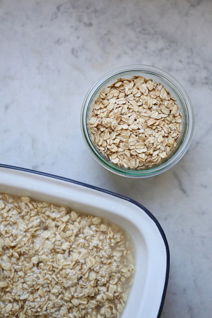 A jar of organic oats and softened oats in an enamel dish on a marble surface