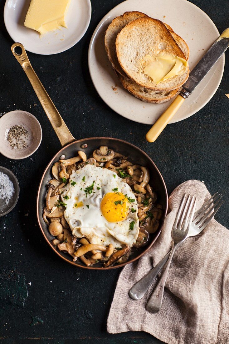 Fried mushrooms with a fried egg in a pan served with toast and butter