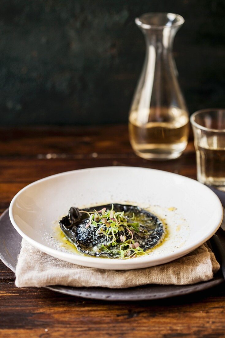 A giant black ravioli in brown butter with cress