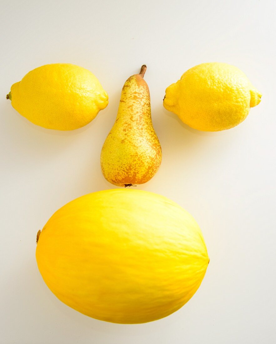 A face made of yellow fruits on a white surface