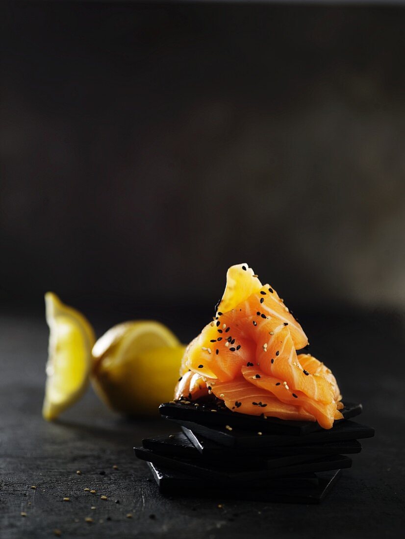 A piece of salmon with sesame seeds on a slate platter with lemon wedges behind it